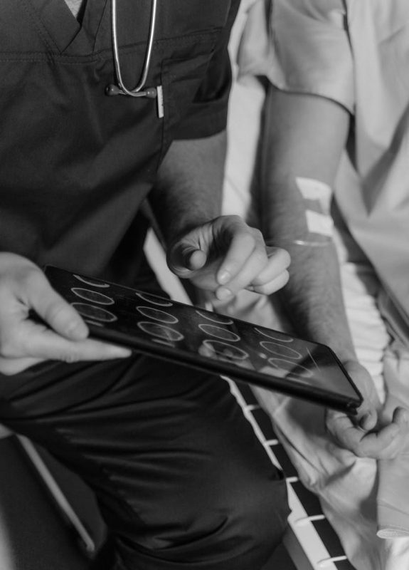 A doctor uses a tablet to show a CT scan to a patient in a hospital setting.